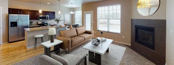 A modern living room with a fireplace and a kitchen area in the background.