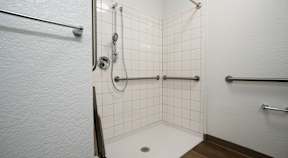 A white tiled shower with a drain in the middle.