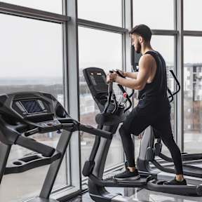 A man is running on a treadmill in a brightly lit room with large windows.