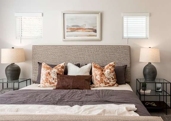 A bed with a grey headboard and a white blanket is flanked by two table lamps.