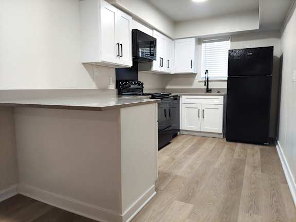 an empty kitchen with white cabinets and a black refrigerator