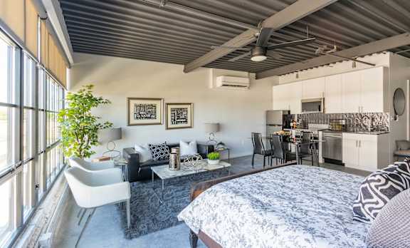 A bedroom with a large bed and a kitchen area in the background.