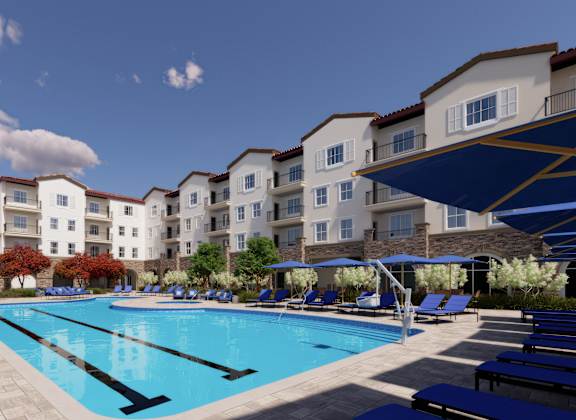 A large swimming pool is surrounded by sun loungers and apartment buildings.