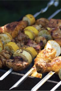 A close up of skewers of chicken and potatoes grilling.