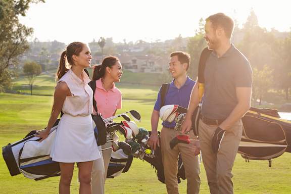 A man and two women are standing on a golf course, with the man holding a golf bag.