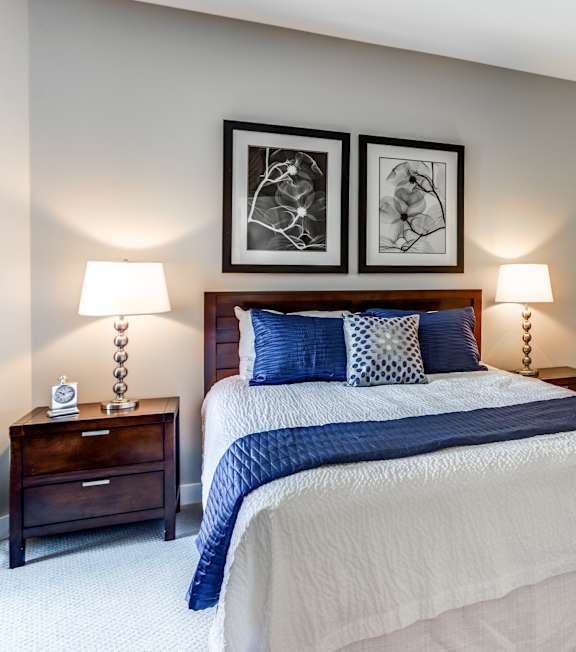 A bedroom with a bed, nightstands, and two wall lamps.