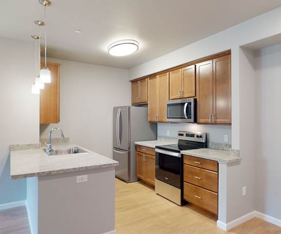 A large kitchen with stainless steel appliances, marble countertop with ample space, and large wooden cabinets at LIVEasy Apartments. 