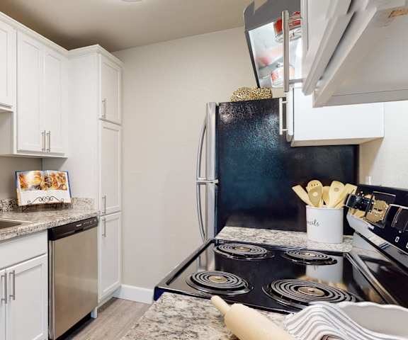 A large, modern kitchen with stainless steel appliances, kitchen utensils, marble countertops with lots of room, and large white wooden cabinets at the Cove Apartment Homes. 