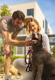 A man and woman petting a dog in front of a house.