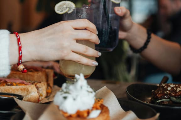 a couple of people holding drinks at a table with food