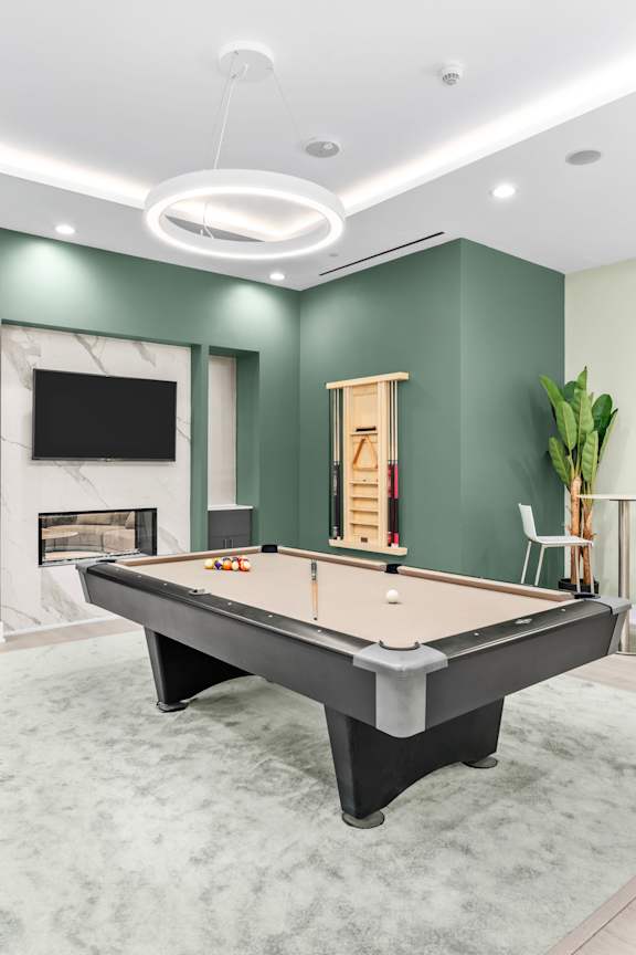 A pool table is in the middle of a room with a fireplace and a TV mounted on the wall.
