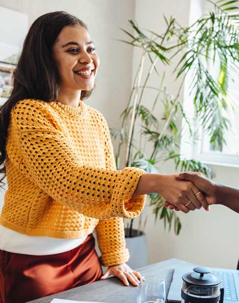 A woman in a yellow sweater shakes hands with a man in a grey sweater.