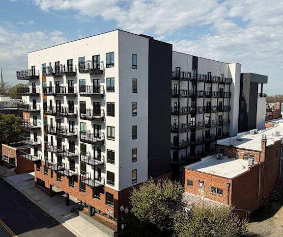 A modern apartment building with balconies is surrounded by other buildings.