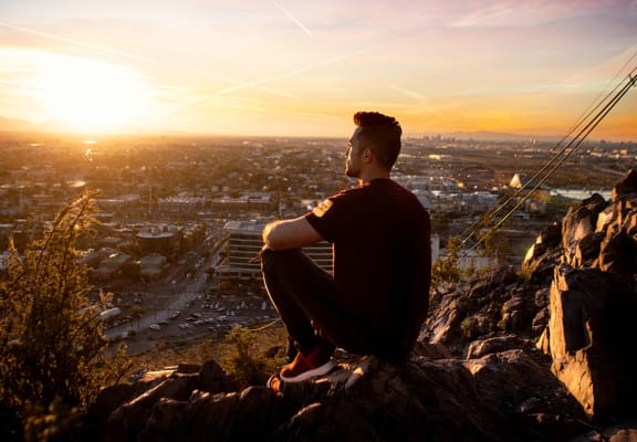 a man sitting on a rock overlooking a city at sunset