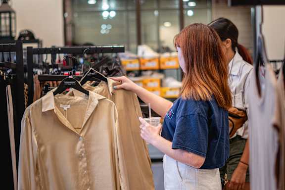 A woman is looking at a beige blouse on a hanger.