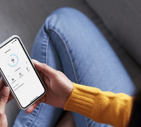 A person in a yellow sweater is holding a smartphone displaying a temperature gauge.