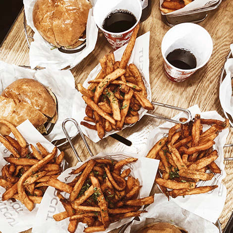 Beer battered fries and burgers on a wood table surrounded by beers.