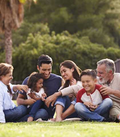 A family of five is sitting on the grass in a park.