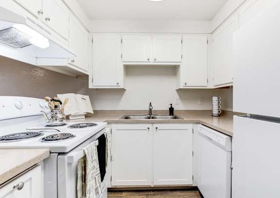 A white kitchen with a stove, sink, and cabinets.