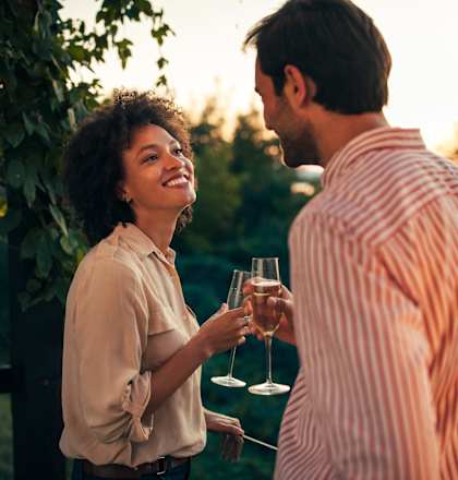 A man and a woman are standing close to each other, holding wine glasses and enjoying a conversation.