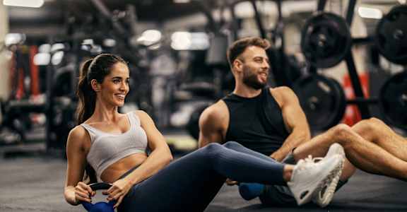 A man and a woman are working out in a gym.