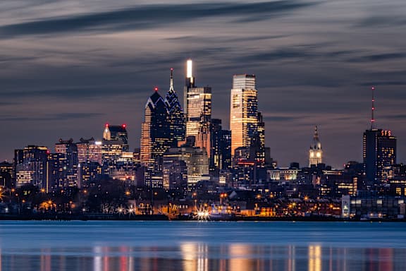 A city skyline at dusk with buildings reflecting in the water.