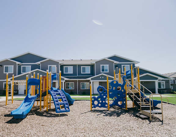 A playground with a blue slide and a yellow slide in front of a building.