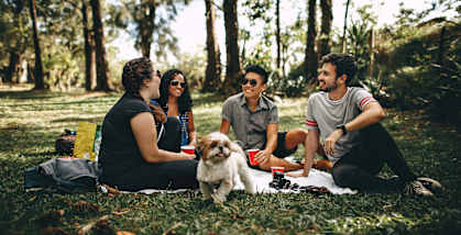 A group of people are sitting on a blanket in a park with a dog.
