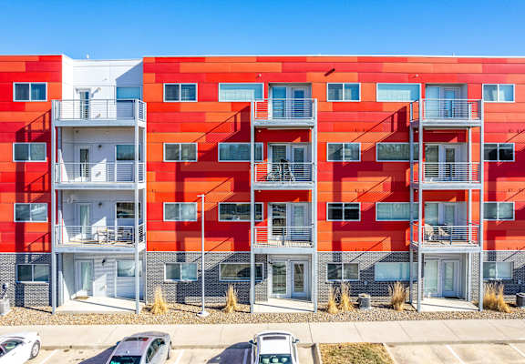 a red apartment building with balconies and cars in front of it