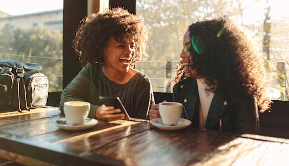Two people sitting at a table with cups of coffee and one person holding a phone. at The Foundry Apartments, Bordon, GU35 9FE