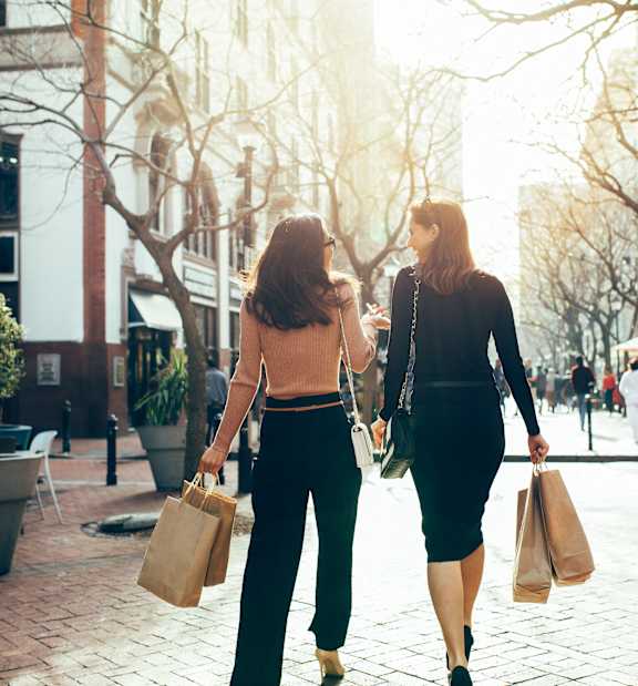 Two women with shopping bags are standing outside a store.