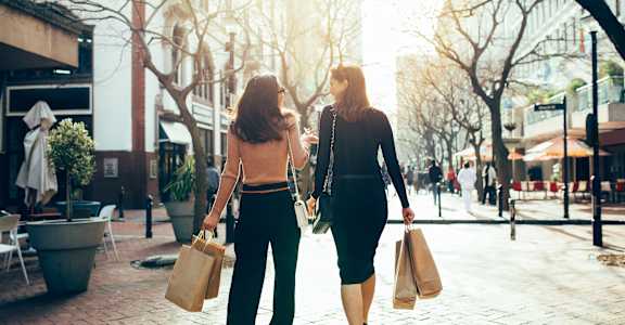 Two women walking down a street carrying shopping bags.