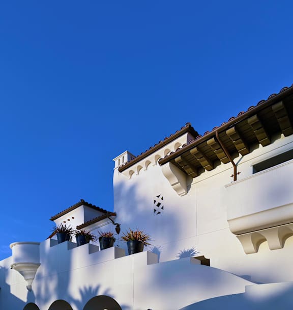 A white building with a red tile roof and a balcony with plants.