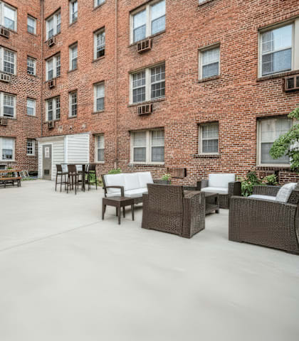 A patio area with wicker furniture and a fire pit in front of a brick building.
