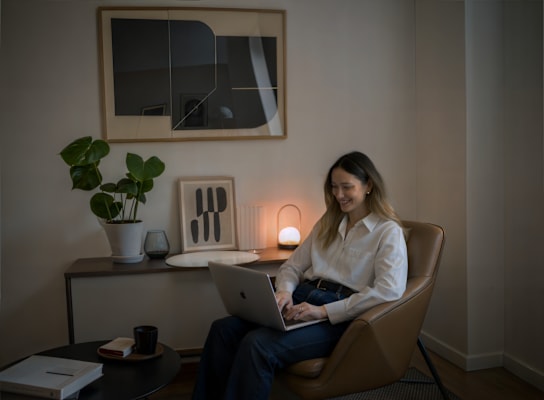 A woman is sitting in a chair with a laptop on her lap.