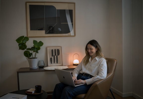 A woman is sitting in a chair with a laptop on her lap.