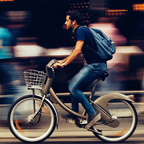A man riding his bike down a busy street listening to music.