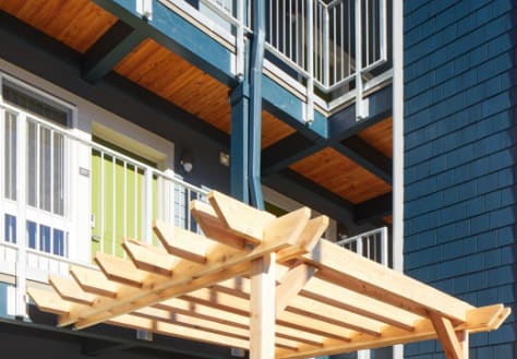 A wooden pergola is in front of a blue building.