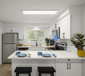 a kitchen with white cabinets and a white island with two black stools in front of it