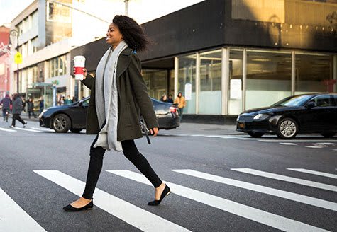 a woman crossing a street holding a cup of coffee
