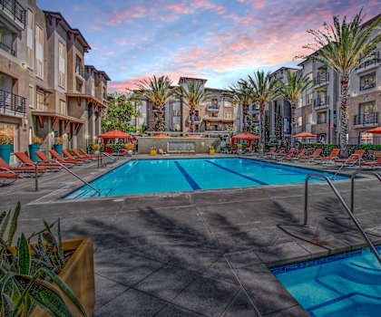 A swimming pool with chaise lounge chairs and umbrellas in front of Artisan at Main Street Metro. 