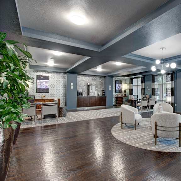 A large clubhouse with chairs and tables and a round rug and a coffee station at Artisan at Main Street Metro.