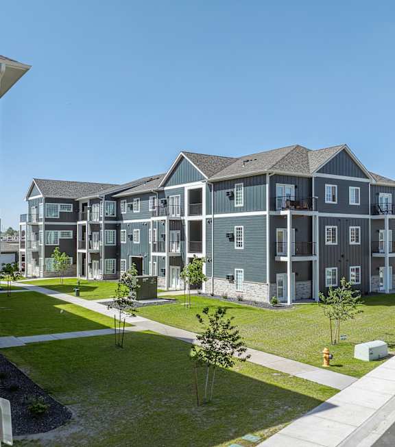 A row of modern townhouses with green lawns and trees in front.