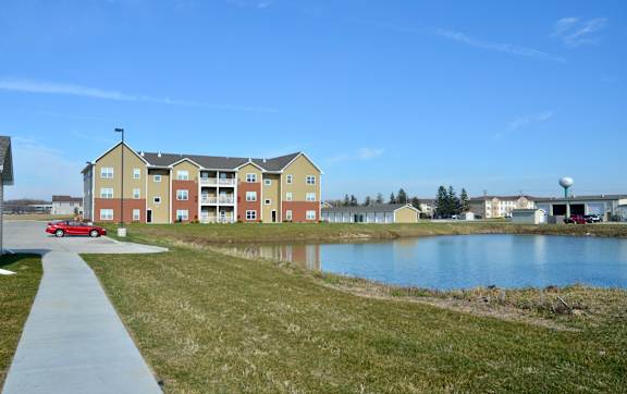 A red car is parked on the side of a road near a grassy area. at Deer Valley Apartments, Silvis, IL, 61282
