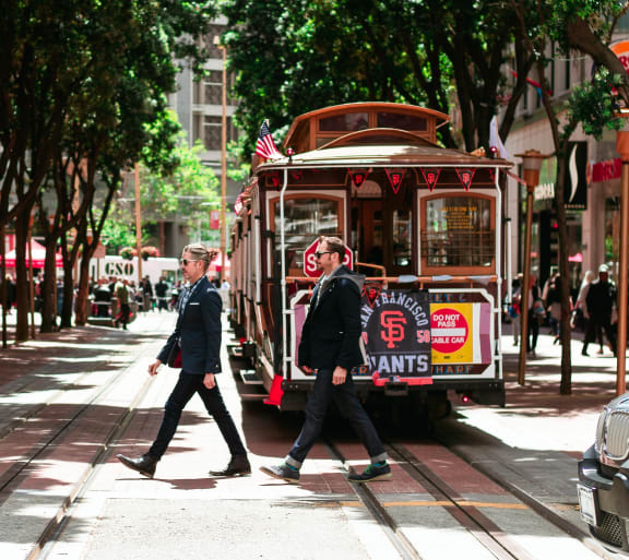 two men crossing the street in front of a streetcar