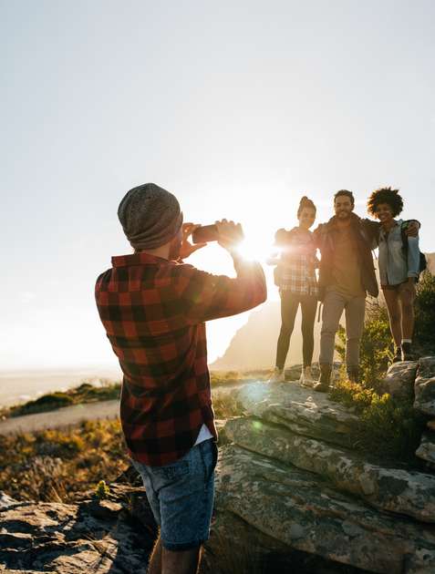 A group of people standing on a rocky hillside with the sun shining brightly in the background.
