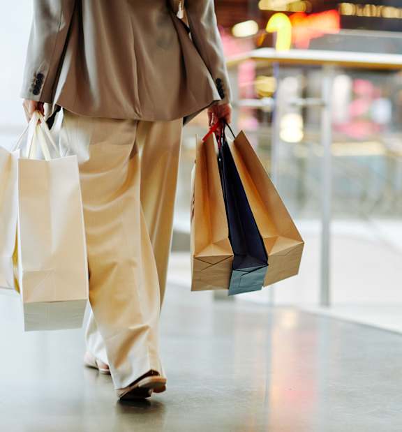 A person in a beige outfit is carrying shopping bags.