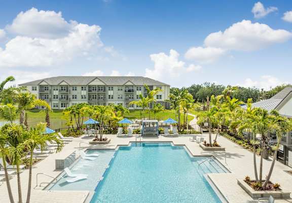 a large swimming pool with palm trees and a building in the background