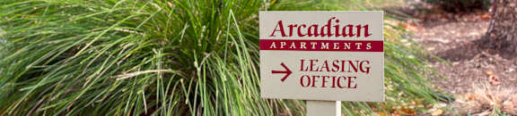 A sign for Arcadian Apartments leasing office is in front of some plants.