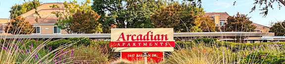 A sign for Arcadian Apartments is in the foreground of a grassy area.